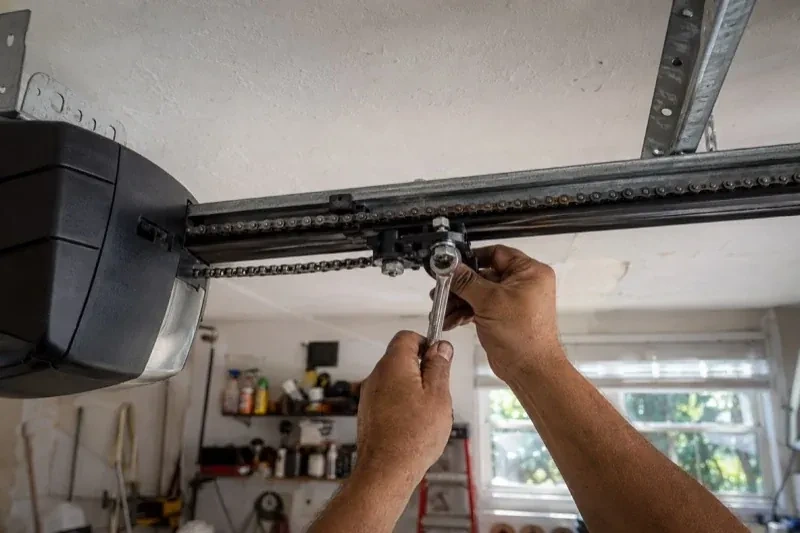 Hands holding a wrench against an opener trolley beneath a chain rail — Chain-Drive Opener Repair, Toronto